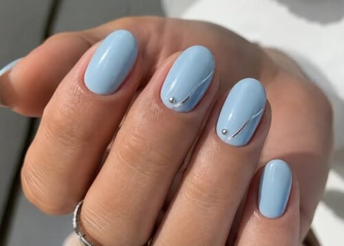 Manicure estiva con smalto azzurro e decorazioni minimal in argento su unghie ovali, elegante e raffinata.