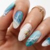 Mano con nail art effetto mare realistica, sfumature azzurre e blu, conchiglia tridimensionale e dettagli che ricordano la schiuma delle onde su sfondo bianco.